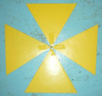 Imagen de una representaci&oacute;n geom&eacute;trica con cuatro tri&aacute;ngulos amarillos dispuestos en forma de cruz sobre un fondo azul texturizado, con el punto central de intersecci&oacute;n iluminado, evocando una estrella en el firmamento.