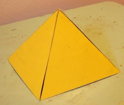 Modelo de pir&aacute;mide triangular amarilla en el primer plano, reposando sobre una superficie desgastada.
