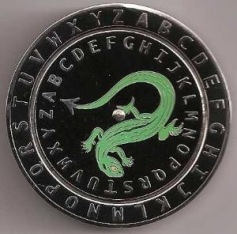 Imagen de una moneda circular con un dise&ntilde;o que incluye un reptil verde serpenteante situado sobre un fondo negro. La moneda est&aacute; rodeada por el alfabeto en letras may&uacute;sculas, grabadas desde la 'A' hasta la 'Z'.
