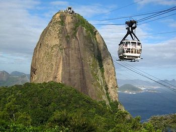Una imagen del telef&eacute;rico que asciende al pico de granito rodeado de vegetaci&oacute;n exuberante, con un paisaje de monta&ntilde;as y oc&eacute;ano al fondo bajo un cielo parcialmente nublado.
