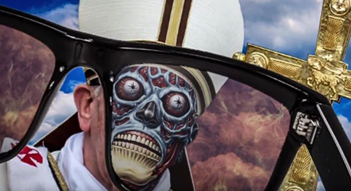 Imagen superpuesta donde se muestra la silueta de unas gafas de sol grandes, que enmarcan una escena surrealista donde aparece un cr&aacute;neo pintado con dise&ntilde;o de calavera en el rostro de un hombre con vestimentas de obispo, incluyendo una mitra blanca. En el fondo, se vislumbran nubes y una cruz dorada en la esquina superior derecha. Interner Link zu einem Artikel auf dieser Website.