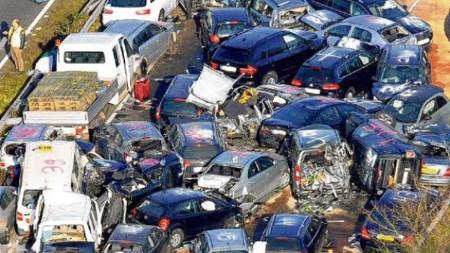 Imagen de un gran accidente de tr&aacute;fico con m&uacute;ltiples veh&iacute;culos involucrados, incluyendo coches y una furgoneta, apilados y da&ntilde;ados en una carretera.