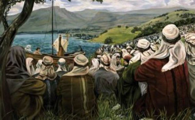 Imagen de una ense&ntilde;anza b&iacute;blica junto a un lago, donde una figura central expone desde una peque&ntilde;a embarcaci&oacute;n a un gran grupo de personas atentas ubicadas en la orilla. El entorno es de colinas verdes y un cielo claro que invita a la contemplaci&oacute;n celestial.