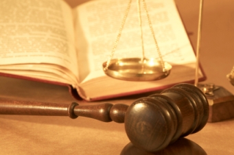 Una imagen que muestra un martillo de juez de madera, balanza de justicia en equilibrio, y un libro abierto sobre un escritorio, enfatizando elementos de la justicia y la ley.