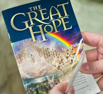 Una mano sostiene un libro titulado "The Great Hope", que muestra una ilustraci&oacute;n de una multitud de personas en un paisaje luminoso con un arco&iacute;ris en el cielo.