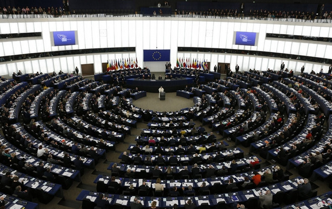 Vista panor&aacute;mica del hemiciclo del Parlamento Europeo durante una sesi&oacute;n plenaria, mostrando a los eurodiputados sentados en formaci&oacute;n semicircular alrededor del orador central. Las banderas de los estados miembros de la UE est&aacute;n al frente.