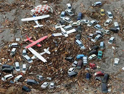 Imagen a&eacute;rea de una colecci&oacute;n de coches en miniatura y dos aviones m&aacute;s grandes sobre un fondo de escombros y ramas, representando quiz&aacute;s una catastr&oacute;fica dispersi&oacute;n terrestre.