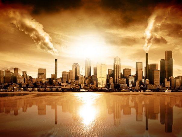 Panorama urbano al atardecer, reflej&aacute;ndose sobre un gran cuerpo de agua, con rascacielos y chimeneas industriales que emiten humo en un cielo te&ntilde;ido de naranja y amarillo.