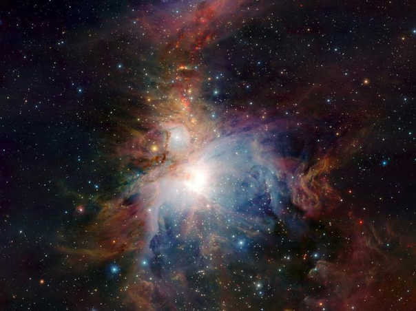 Imagen de una nebulosa en detalle con tonalidades de azul, naranja y blanco, destacando un brillante centro lum&iacute;nico rodeado de nubes de gas y polvo interestelar.