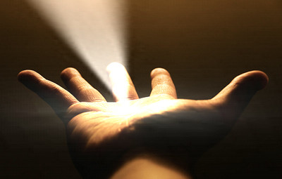 Una mano abierta hacia arriba que atrapa un haz de luz brillante sobre un fondo oscuro, sugiriendo un sentido de descubrimiento o revelaci&oacute;n.