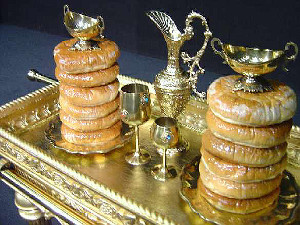 Una bandeja dorada con pilas de roscas glaseadas acompa&ntilde;adas de copas y jarritas met&aacute;licas decorativas.
