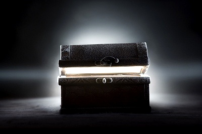 Una imagen de dos libros antiguos apilados, uno sobre el otro, ambos cerrados con resplandor luminoso emergiendo de entre ellos, evocando un misterio celestial. La escena est&aacute; ba&ntilde;ada en una suave luz cenital que tambi&eacute;n ilumina un fondo oscuro y difuso.