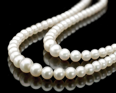 Un conjunto de collares de perlas naturales con superficies brillantes y lisas, reposando sobre un fondo negro que refleja su imagen.