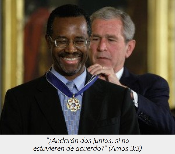 Un hombre afroamericano sonriente recibe una medalla de un hombre cauc&aacute;sico mayor que lo observa con aprecio. Ambos est&aacute;n vestidos formalmente en un evento ceremonial.