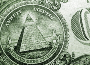 Imagen en primer plano de un billete con un s&iacute;mbolo de una pir&aacute;mide con un ojo que todo lo ve en la c&uacute;spide, rodeado de inscripciones latinas. A la derecha se vislumbra parte de un dise&ntilde;o de c&iacute;rculos conc&eacute;ntricos que podr&iacute;a representar cuerpos celestes.