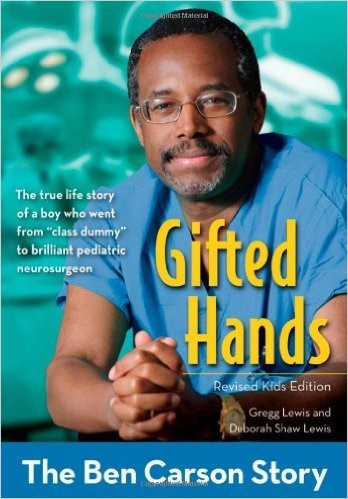 Portada del libro "Gifted Hands: The Ben Carson Story," que muestra a un hombre afroamericano con gafas y scrubs quir&uacute;rgicos azules, posando con los brazos cruzados y una expresi&oacute;n pensativa. El fondo es verde con im&aacute;genes superpuestas de cerebros y formulaciones m&eacute;dicas.
