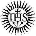Imagen de un s&iacute;mbolo solar con rayos extendidos y las letras IHS entrelazadas en el centro, sobre un fondo blanco.